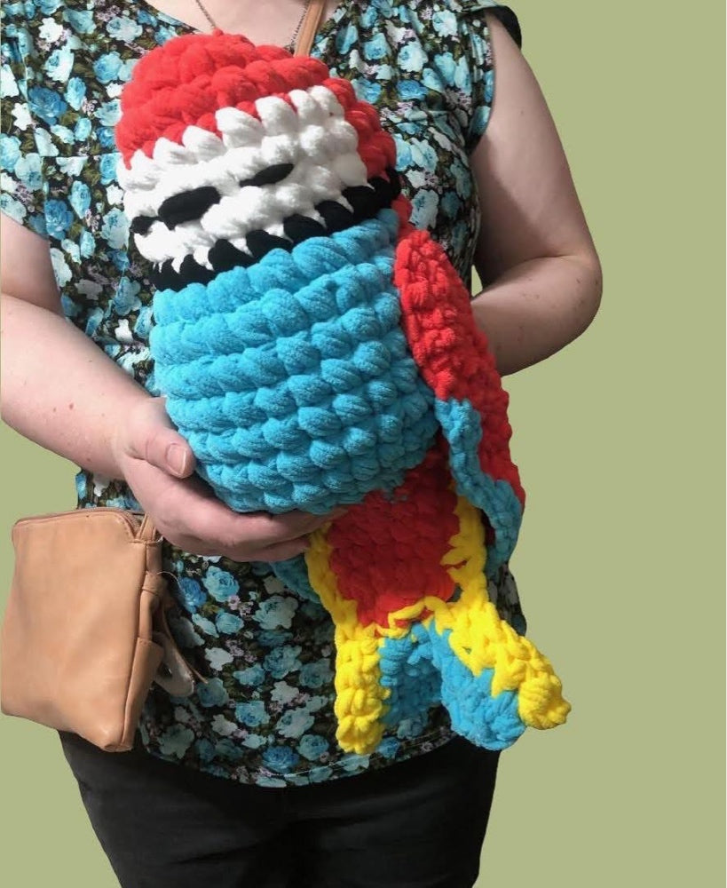 A large red, white, and blue bird with sleepy eyes and intricate yellow and blue tail feathers. It is being hugged by a person.