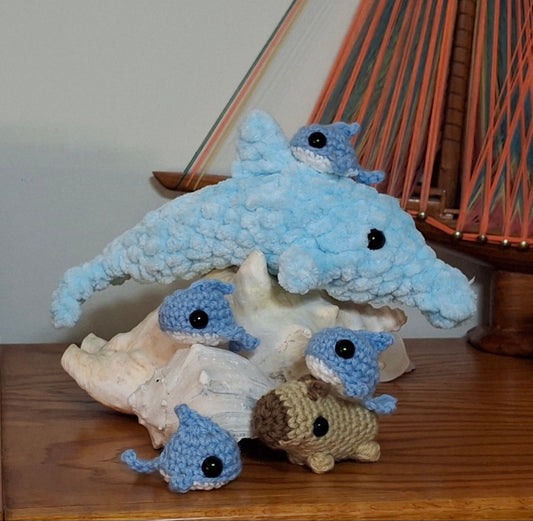 A family of plush crochet dolphins in bright blue, accompanied by a small brown capybara friend.