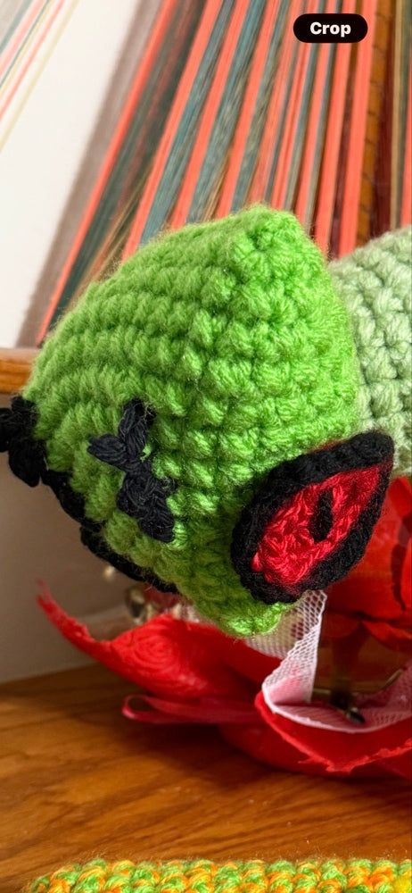 Close-up of a crochet praying mantis head showing intricate green stitching and large, hand sculpted red eyes.